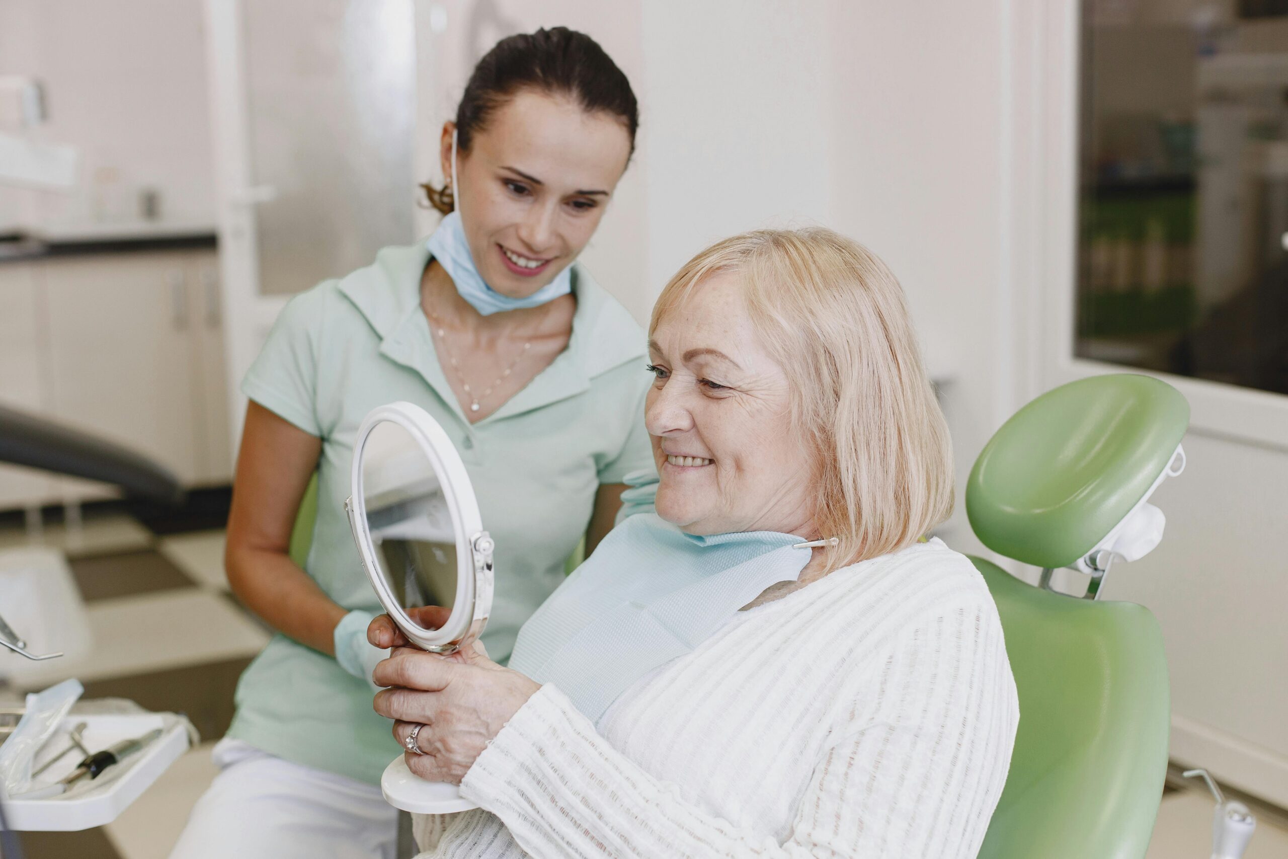Senior woman smiles while checking her teeth in a mirror with a dentist. Healthcare and dentistry concept.