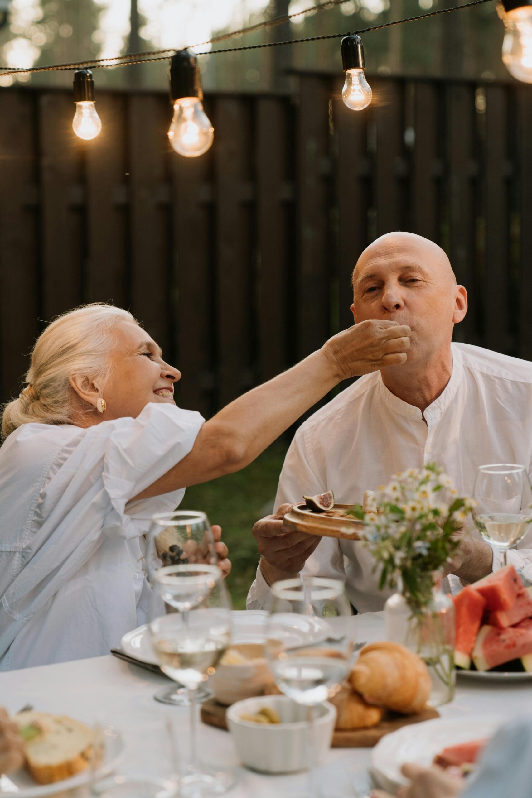 Elderly couple sharing a happy dining moment outdoors with warm lighting and delicious food.
